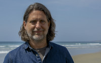 A man with shoulder-length hair stands at the beach