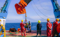 Workers in hard hats and jump suits deploying mooring from research vessel.