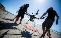 Researchers with Adam Young carrying a LIDAR drone on the beach.