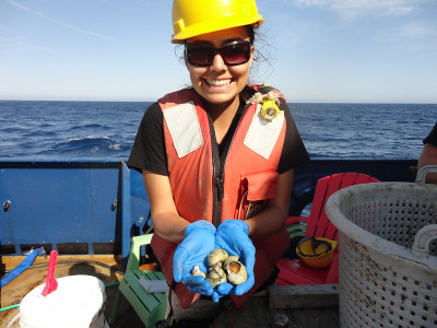 A female student aboard a research vessel holds marine specimens in her cupped hands
