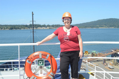 A woman in a hard hat and red shirt stands on a boat