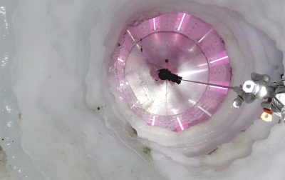 Peering into an icy borehole, lit up in pink UV lights
