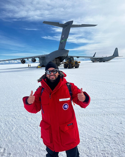 A researcher in a red jacket in Antarctica, with a plane in the background