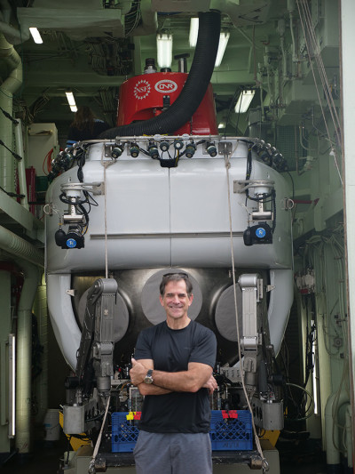 A man on a ship stands in front of a deep-sea submersible