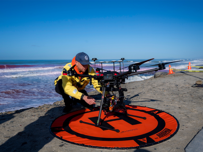 A man prepares to launch a drone at the beach.