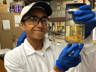 A young man in a lab holds a jar with a marine specimen