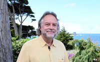 Portrait of a man in a yellow shirt near a tree; the ocean is seen in the background