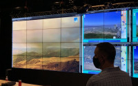 A man in front of a series of video screens displaying wildfire information