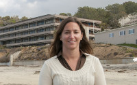 A woman stands on the beach; a research building in shown in the background