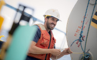 An oceanographer wearing a safety hat and life jacket conducts research on a ship