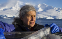 Portrait of a woman scientist on a boat in Antarctica; an iceberg is seen in the background