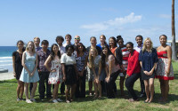 Group photo of students gathered on a lawn near the ocean.