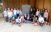 Group photo of college students standing in front of a wood-paneled building.