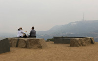 Two people sitting on a bench in smoky air overlooking Hollywood sign.