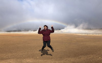 Woman jumping in field with rainbow in background.