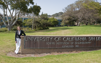 A woman leans against a campus entrance sign for Scripps Institution of Oceanography