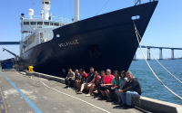 People sit in front of a docked research vessel