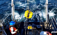 Marine scientists deploy an acoustic instrument off a ship.