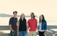 Four graduate students standing on a deck near the ocean.