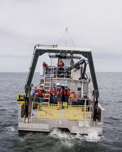 The stern of a small research vessel at sea, with a team of researchers visible.