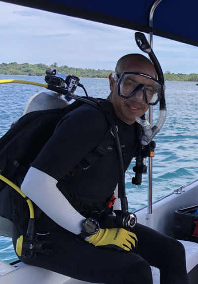 A man in scuba diving gear sits on the edge of a boat