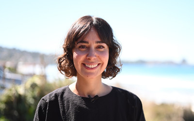 Portrait of a smiling woman with short brown hair, a beach is visible in the background