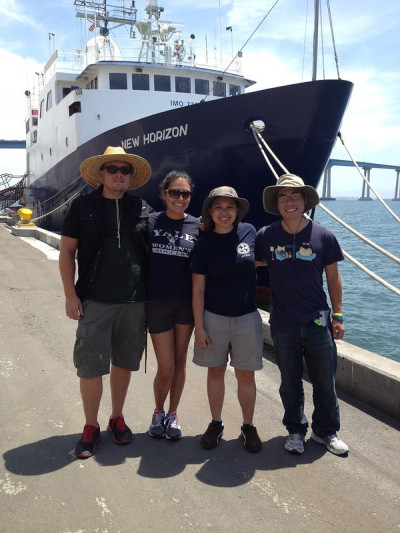 Four people at a dock stand in front of a large research vessel, R/V New Horizon