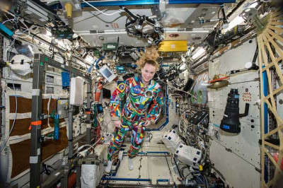 A female astroanut in a colorfu suit floats inside the Space Station.