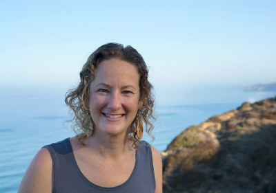 Portrait of a woman with curly blonde hair and the ocean/cliffs in the background