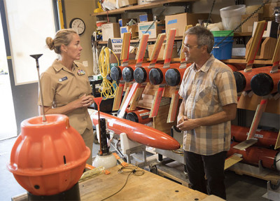 A woman and man stand in a research lab filled with bright orange oceanographic instruments.