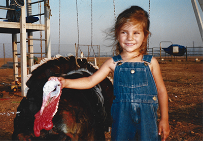 A young girlin overalls pets a turkey.