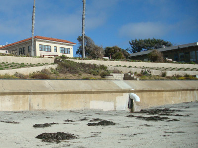White pipe protruding from embankment above beach sand.
