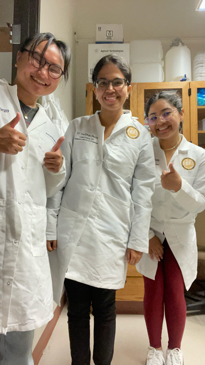 Three researchers in lab coats and protective glasses in a lab.