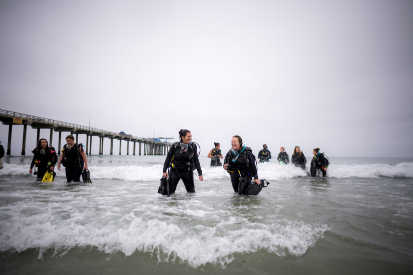 A group of student divers emerge from the water near a research pier.