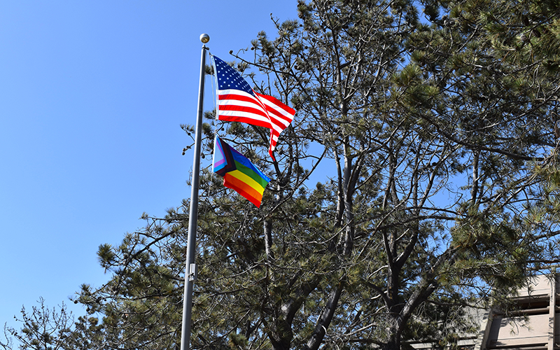 An American flag and a Progress Pride flag wave from a flagpole.