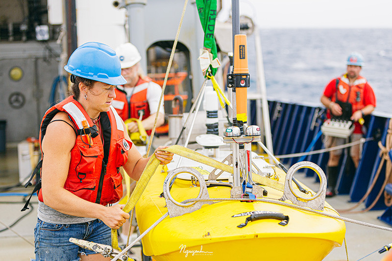 Female researcher securing line on equipment on deck of research vessel.