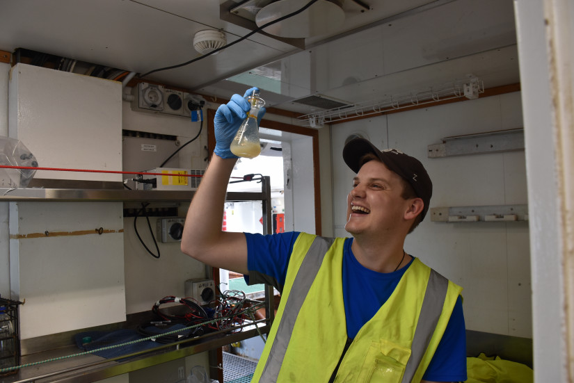 Mitchell Chandler poses onboard NIWA's R/V Tangaroa with a water sample collected from thousands of metres deep that will be analysed to measure the dissolved oxygen content of the seawater. Photo: Steve Diggs