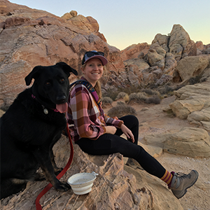 A woman in hiking gear outdoors with her dog
