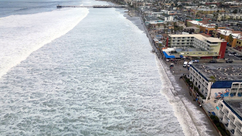 Waves top the boardwalk at Mission Beach, San Diego during a king tide in December 2023.