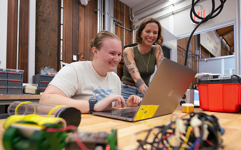 Two women look at the screen of a laptop in a workshop in the Scripps Sandbox Makerspace.