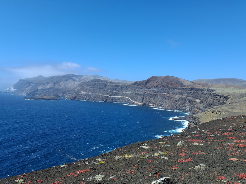 Volcanic strata along the southwestern shore of Guadalupe Island, looking north. Two dark-colored, vertical volcanic dikes are exposed cutting through the strata along the cliff face and previously supplied lava to scoria cones and lava flows at the surface.