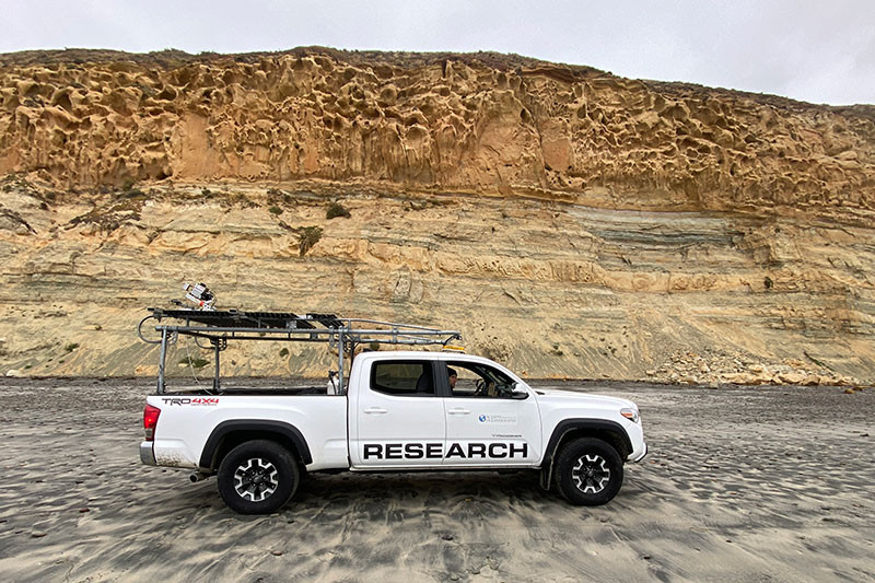 White pickup truck on beach in front of Torrey Pines cliff face.
